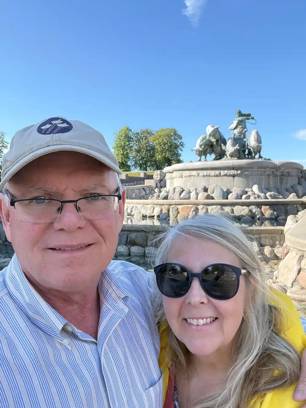 Couple posing before stone equestrian monument under blue sky
