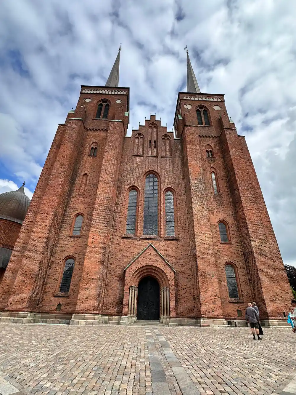 Red brick church with twin spires and cloudy sky