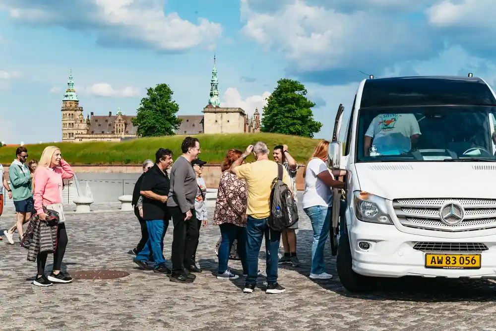 Tour group boarding white coach bus near waterside fortification